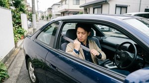 運転席で動かないシートベルトを見つめる男性