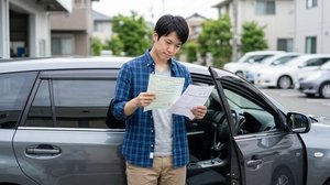 車の横で車検や点検に関する書類を確認する様子