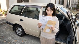 クルマの横で納税通知書を読む女性